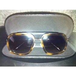 Et par store, firkantede solbriller i skildpaddeskjold med mørke glas ligger i et åbent, sort etui.